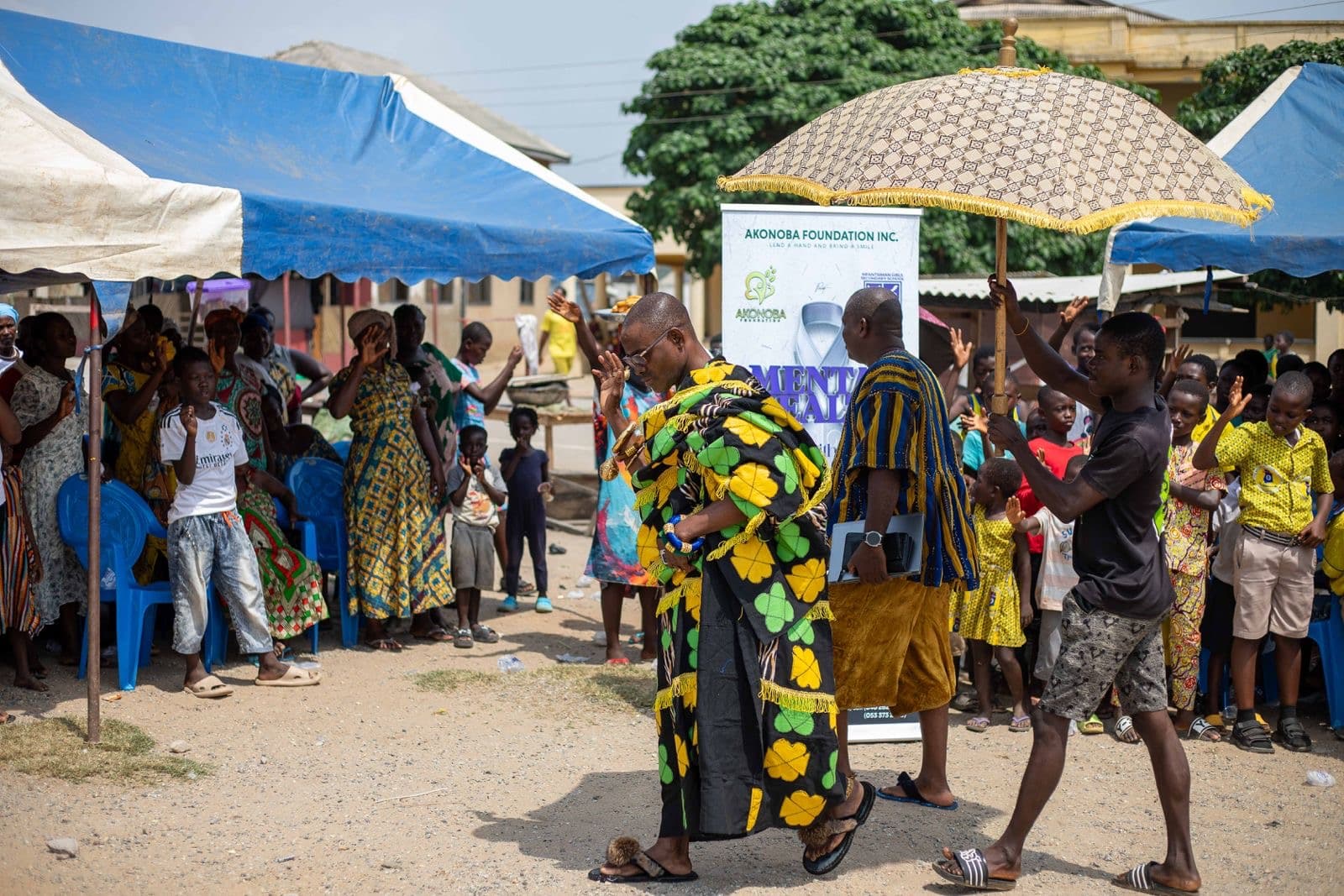 A large outdoor community gathering hosted by Akonoba Foundation, with community members and young people standing together beside the Foundation's mental-health awareness banner.