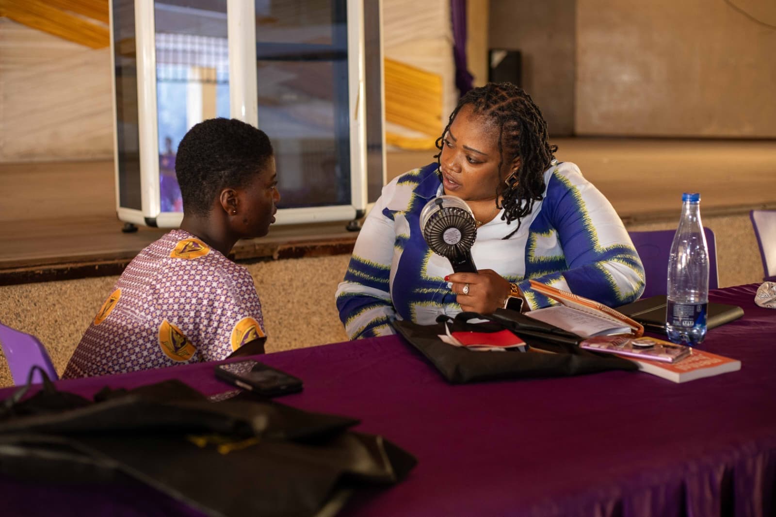 Two people seated at a table in conversation during an Akonoba Foundation outreach session, notebook open between them.